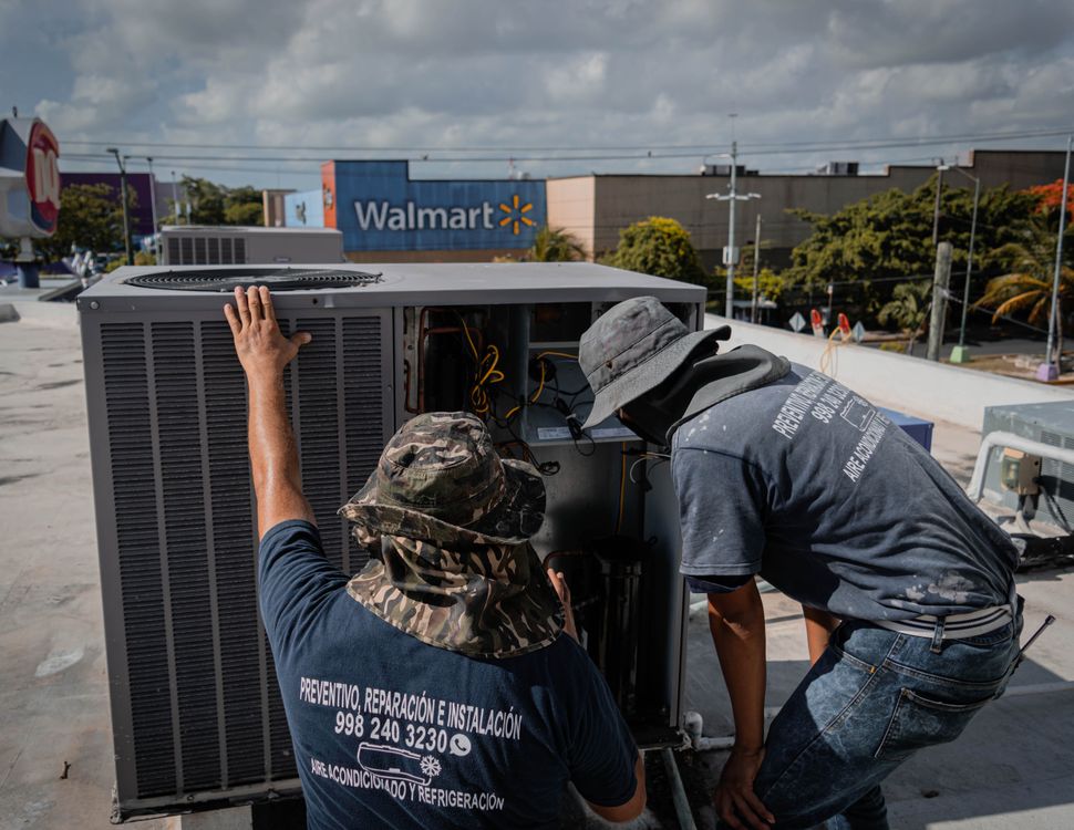 Two technicians in work gear inspecting a rooftop air-conditioning condensing unit during an R-410A recharge