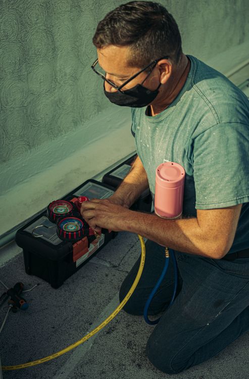 Refrigeration technician servicing an air-conditioning system with specialist recovery and leak-detection tools